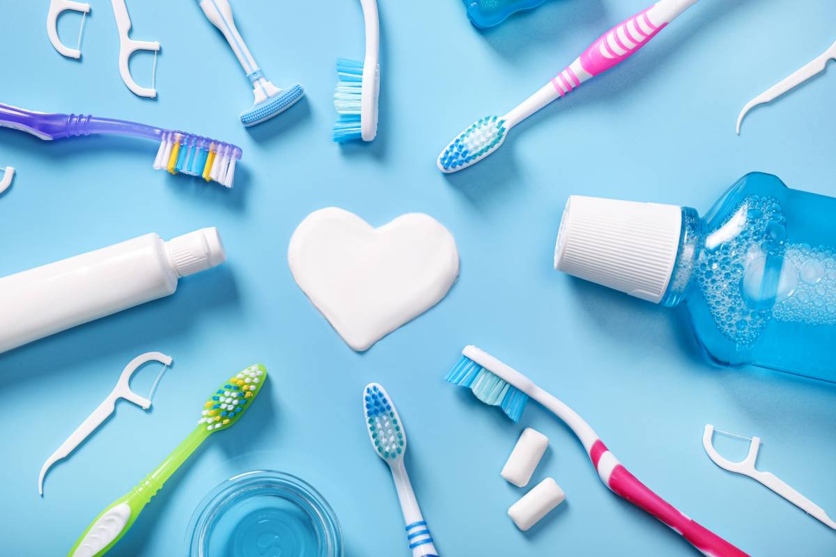 Dental products and toothpaste for gum disease arranged in heart shape on blue background.